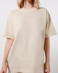 Close-up of a model wearing a beige t-shirt with tonal 'LEGEND' printed on the center chest on a white background