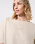 Model wearing an over-sized beige t-shirt with tonal 'LEGEND' printed in teh center of the chest on it against a white background