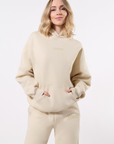 Model wearing a beige hooded sweatsuit with 'LEGEND' in tonal printing on the center of the chest on top left thigh on a white background