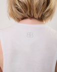 Close-up of a model wearing a white sleeveless top with a gray BB logo on the back of the neck against a neutral background