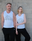 Two models wearing "Make Your Own History' printed in gray on white tank tops paired with black sweatpants with a white printed BB logo leaning against a stone wall