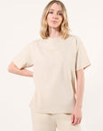 Model wearing a beige t-shirt with tonal printed 'LEGEND' in the center of the chest and tonal 'LEGEND' printed on the thigh of the pants on a white background