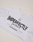 Flat lay of a white, long sleeve boxy tee with "Imperfectly Perfect" screen printed in black on a white backdrop.