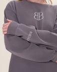 Model is wearing an oversized long sleeve gray t-shirt with a crew neck and white printed BB logo in the center of the chest and Birdiebee printed on the wrist of one sleeve, in front of a white backdrop
