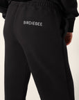 A pair of black oversized sweatpants with 'Birdiebee" printed across the right side a couple of inches below the waistband, featuring a comfortable elastic waistband and pockets in front of a white backdrop