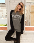 Model wearing a gray shirt with 'IMPERFECTLY Perfect' screenprint standing in front of a window with cityscape background.
