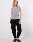 Model wearing a gray crew neck t-shirt with the mantra 'COURAGE OVER COMFORT' printed in black on the center of the chest paired with 'Courage Over Comfort' black pants with white print in front of a white background