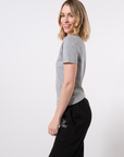 Side-view of a model wearing a gray crew neck t-shirt paired with black, 'COURAGE OVER COMFORT' sweatpants printed in white on the left thigh in front of a white background