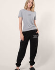 Model wearing a gray tee with black ‘Courge over Comfort” graphic art printed on the center of the chest paired with coordinating black joggers