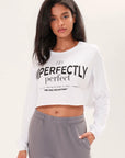 Model wearing a long sleeve white boxy tee that says "Imperfectly Perfect" in black graphic art in front of a white backdrop
