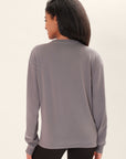 Back-view of a model wearing an oversized long sleeve gray t-shirt with a crew neck with Birdiebee printed on the wrist of one sleeve, in front of a white backdrop