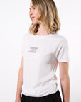 Model wearing a white t-shirt with text 'Courage Over Comfort' printed in black with black sweatpants in front of a white backdrop