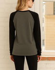 Back view of model wearing sporty raglan tee that is gray and black looking out the window