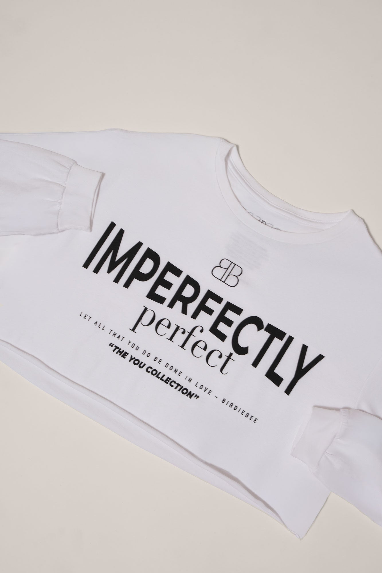 Flat lay of a white, long sleeve boxy tee with "Imperfectly Perfect" screen printed in black on a white backdrop.