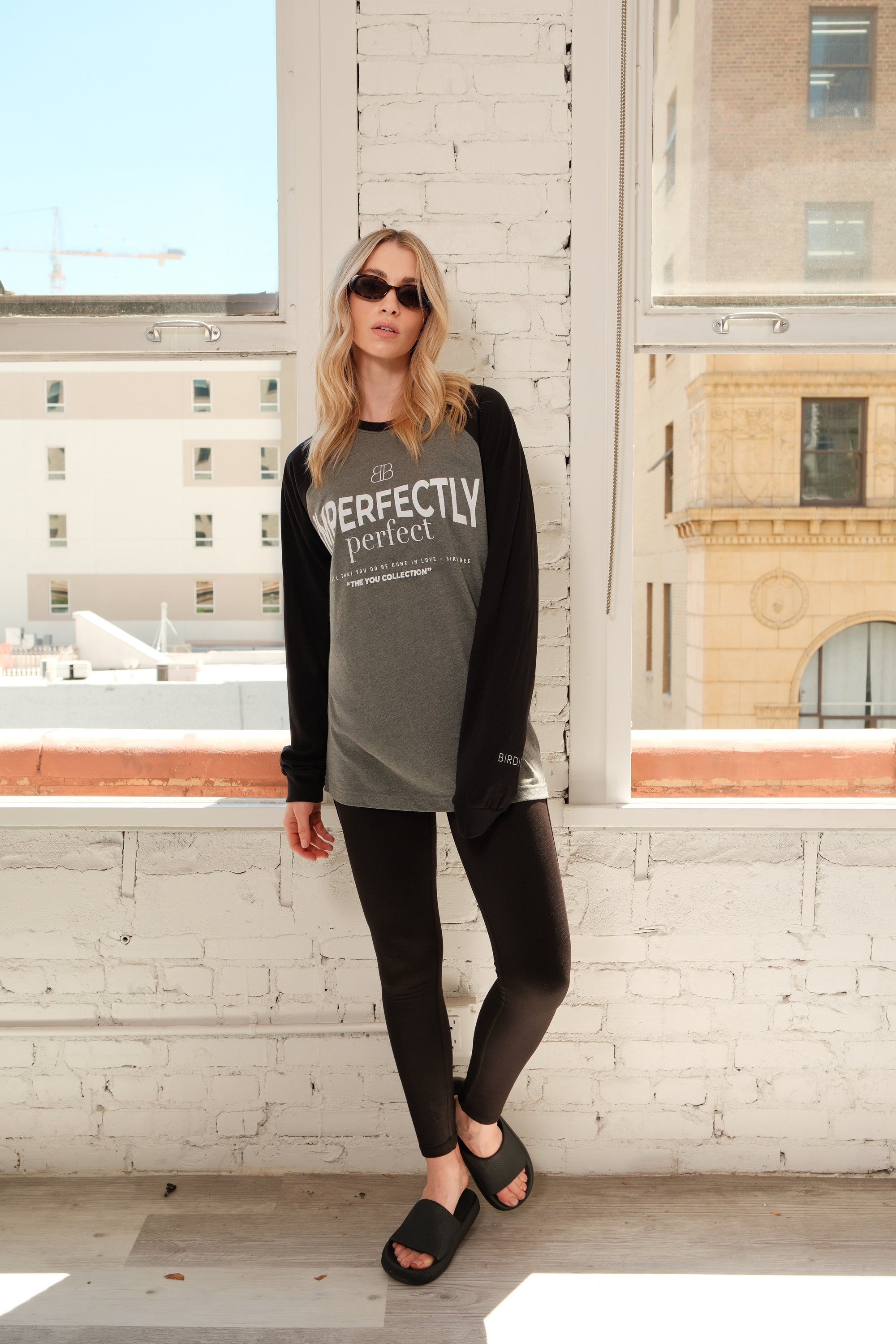 Model wearing a 'IMPERFECTLY Perfect' shirt on a rooftop with cityscape background