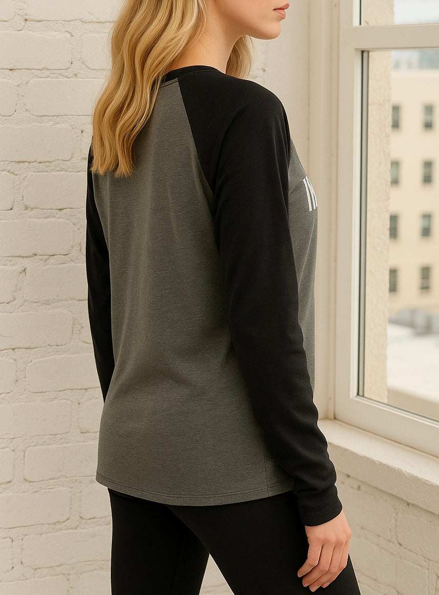 Model wearing a black and gray long-sleeve shirt in front of a window with a cityscape view.
