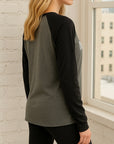Model wearing a black and gray long-sleeve shirt in front of a window with a cityscape view.