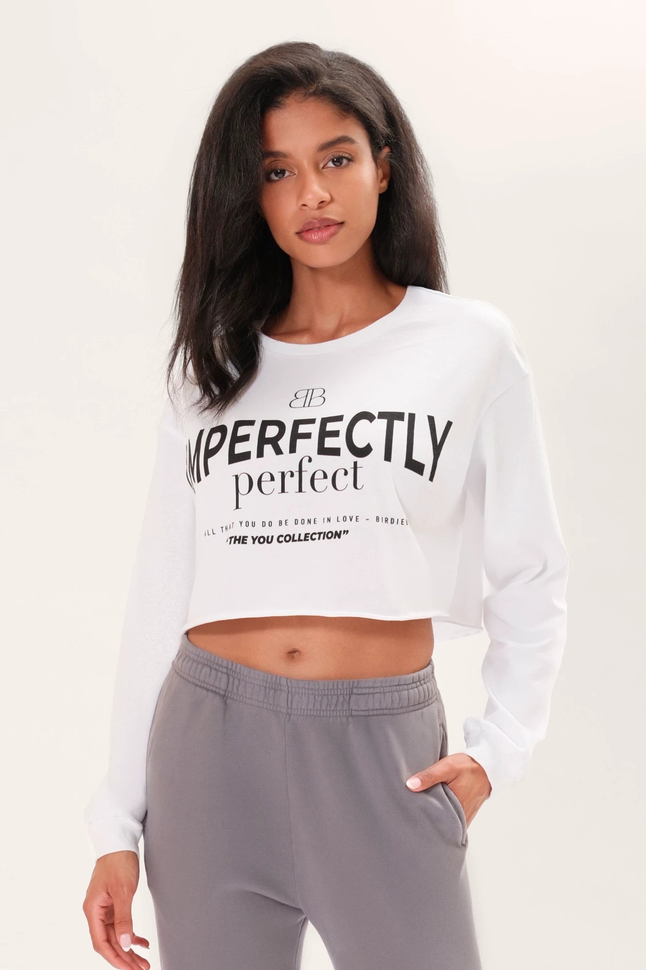 Model wearing a long sleeve white boxy tee that says "Imperfectly Perfect" in black graphic art in front of a white backdrop