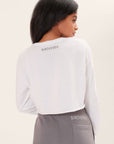 Backv-view of a model wearing a long sleeve white boxy tee with the Birdiebee logo across the bacl of the neck in black graphic art with gray joggers that have the Birdiebee logo above the left back pocket screen-printed in white in front of a white backdrop.